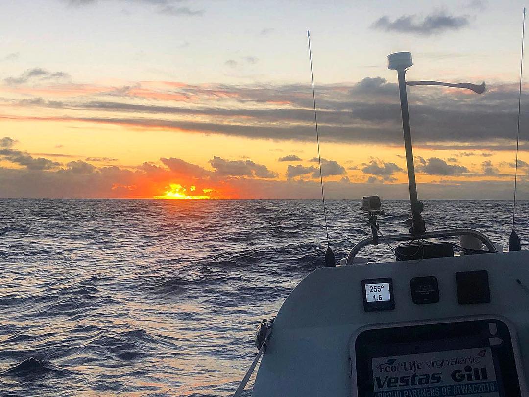 Sunset over open ocean seen from the deck of a small boat with instruments and aerials