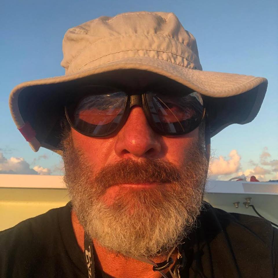 Sunburnt bearded man in a wide brimmed sun hat and sunglasses at sea