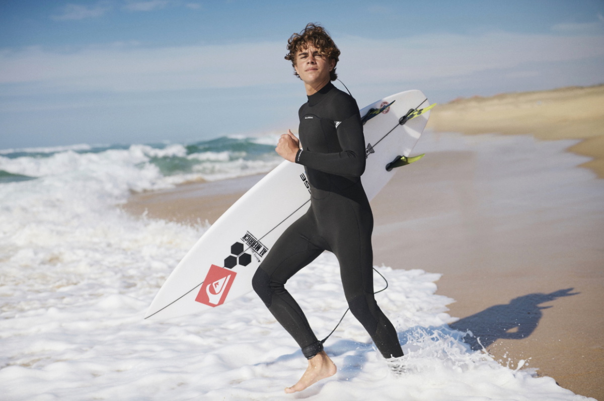 Surfista con traje de neopreno Quiksilver caminando por la playa con su tabla