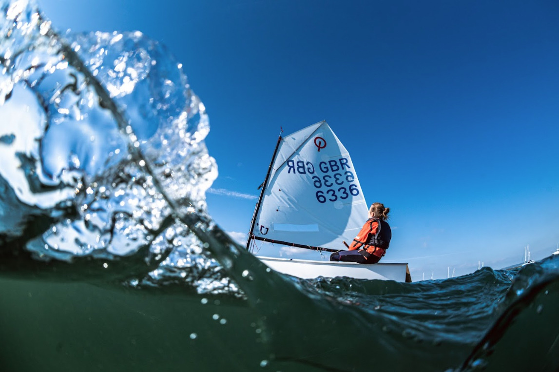Half-underwater shot of a young sailor hiking out in a single-handed dinghy under a blue sky