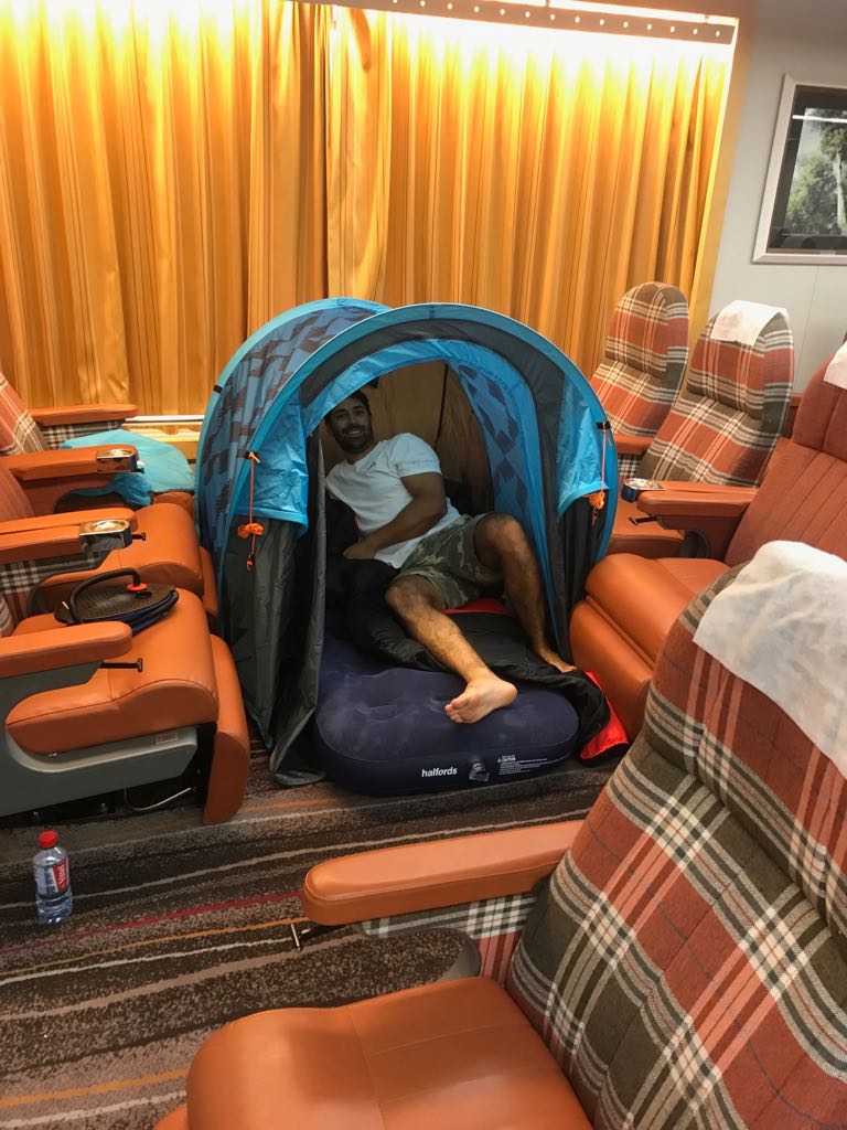 Sailor asleep in a pop-up beach tent pitched across orange lounge seats indoors