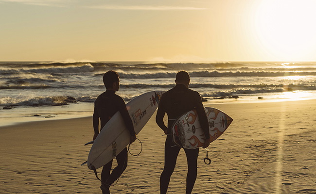 Surfistas con traje de neopreno recortados contra una puesta de sol