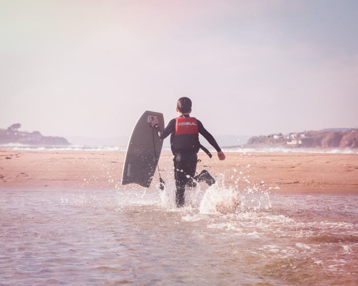 Child running towards the ocean with Gul body board